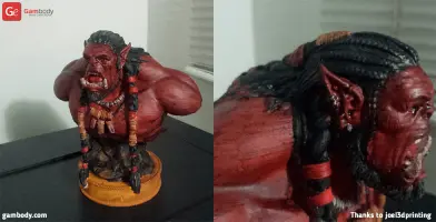 A detailed 3D-printed bust of a fierce, red-skinned orc with braided hair, displayed on a base.