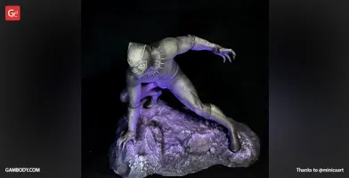 A detailed 3D-printed figure of a superhero crouching on a rocky base, illuminated by purple light.