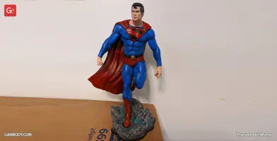 A classic Superman 3D printed model in a blue suit and red cape, standing heroically on a stone base.
