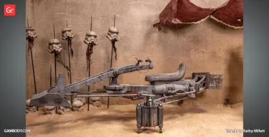 A detailed Mandalorian speeder bike model in a desert setting with helmets on spikes in the background.