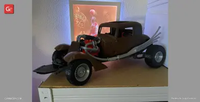 A 3D-printed model of a vintage, modified car with large tires and exposed engine on display.