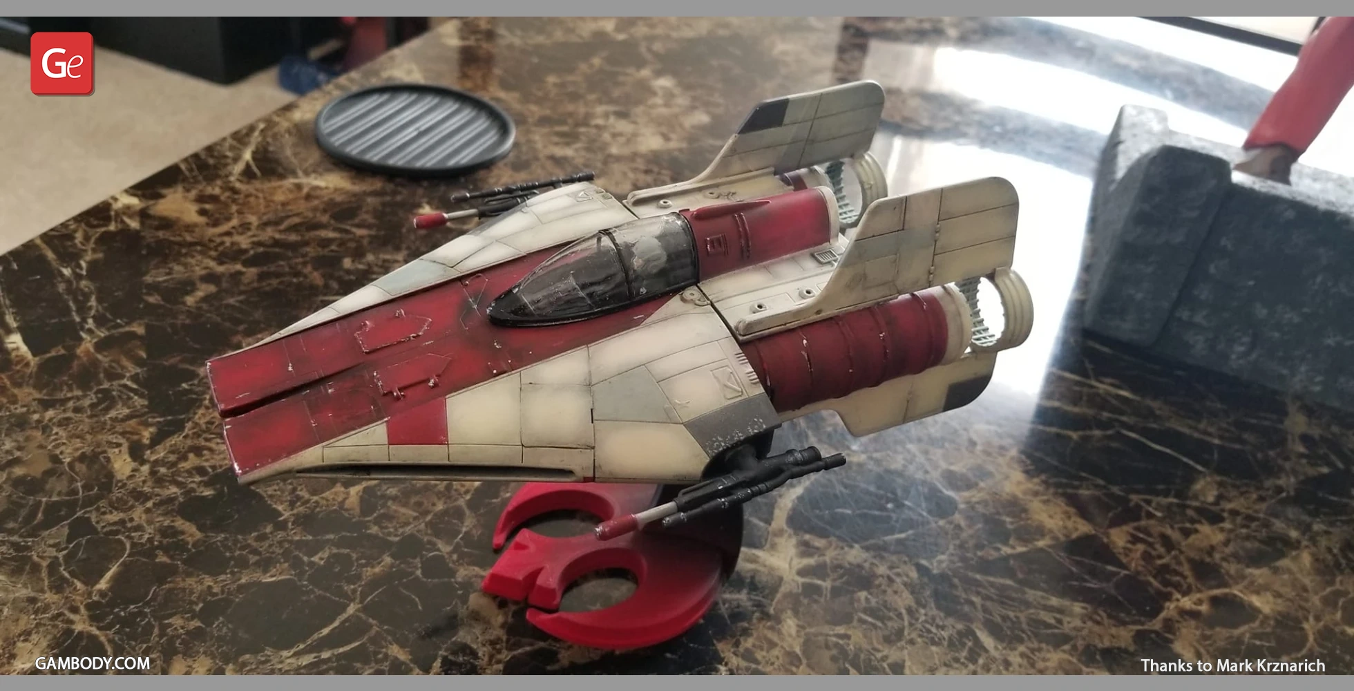 Red and white RZ-1 A-Wing model on a red stand, displayed on a marble surface.