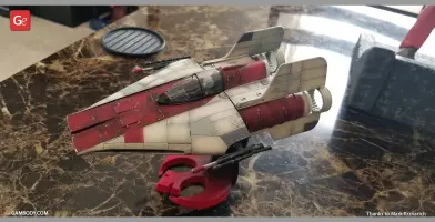 Red and white RZ-1 A-Wing model on a red stand, displayed on a marble surface.
