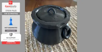Black 3D-printed cauldron with lid and handle on a textured surface.