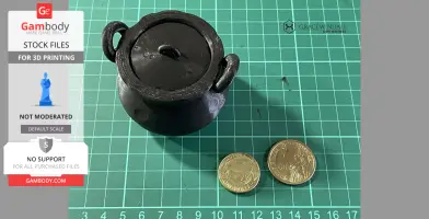 Black 3D-printed cauldron with lid and handles, placed on a grid mat next to two coins for scale.