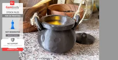 A 3D-printed mini black cauldron with rope handles and a lid, placed on a stone surface.