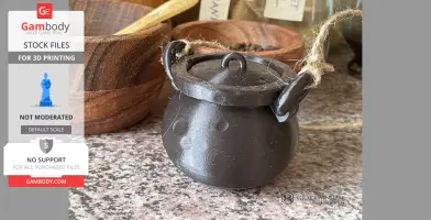 Small 3D-printed black cauldron, textured surface, with handles, on a kitchen counter.