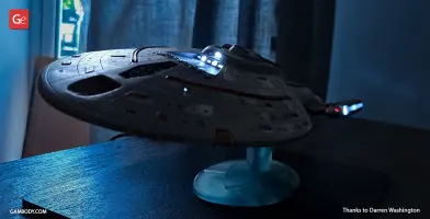 3D printed model of USS Voyager with lit windows and engines, mounted on a display stand.