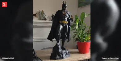 A 3D-printed Batman 1989 model stands on a rocky base, next to a potted plant.