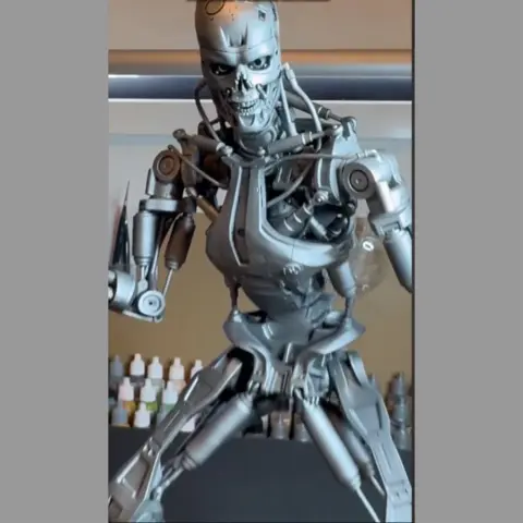 Futuristic robotic endoskeleton standing on a base with skulls and debris.
