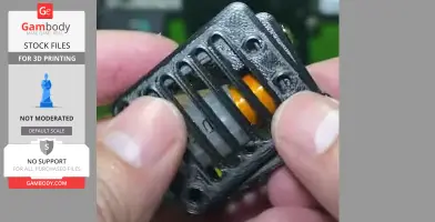 Close-up of hands holding a 3D-printed component with slotted black casing and visible orange parts inside.