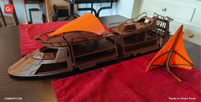 Brown 3D-printed model of a sci-fi sail barge with orange sails on a table.