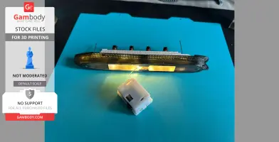 A 3D printed Titanic model with interior lighting on a blue surface, connected to a power source.