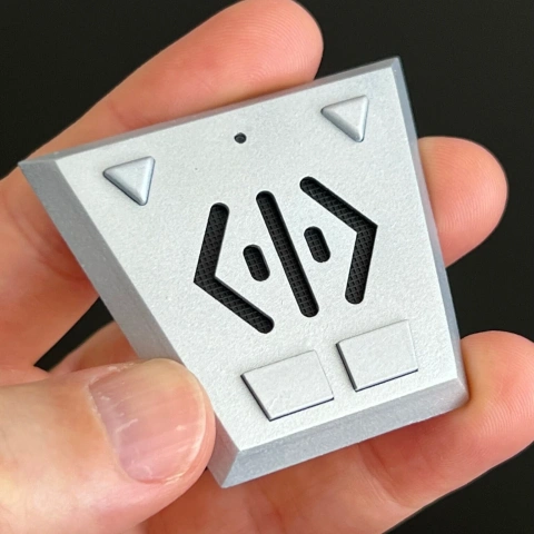 A hand holding a triangular gray comm-link prop with geometric buttons and symbols, inspired by Babylon 5.