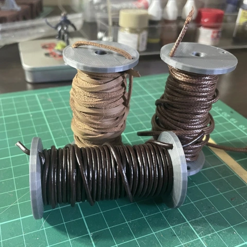 Three large spools wrapped with leather cords on a cutting mat, surrounded by crafting supplies.