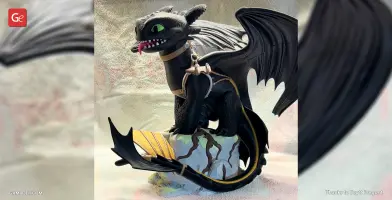 A 3D model of Toothless, the Night Fury dragon, with harness, sitting on a rock.