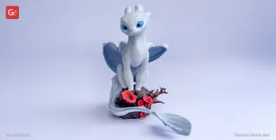 White dragon with blue eyes and wings perched on a rock with red flowers and branches.