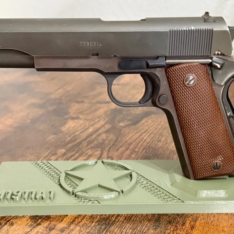 A 1911 pistol displayed on a green WWII-themed stand with a star and textured design.