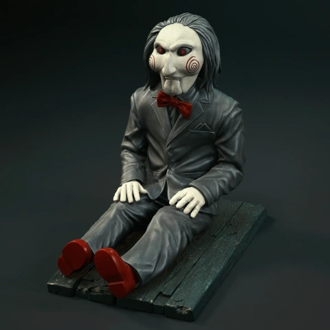 A puppet with a white face, red bow tie, and suit sits on a wooden platform.