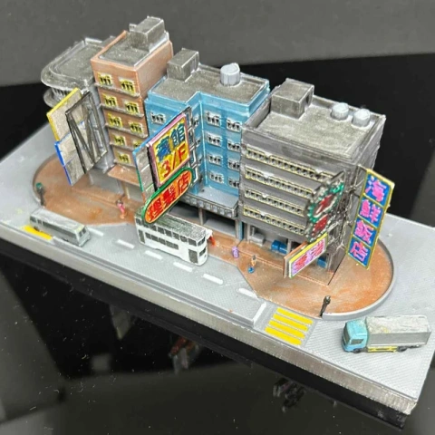 Miniature Hong Kong streetscape with colorful buildings, signs, bus, and tram on a curved road.