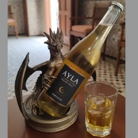 A dragon-shaped wine caddy holds a bottle, next to a glass of chilled drink on a table.
