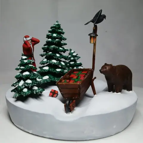 Santa and bear with a lantern, wheelbarrow, and snow-covered trees in a Christmas diorama scene.