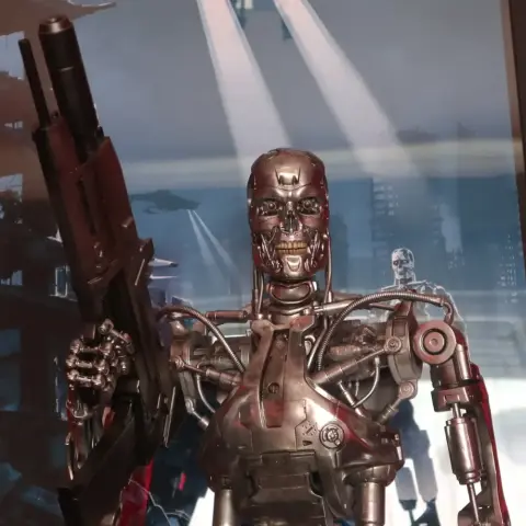 Futuristic humanoid robot endoskeleton with red eyes, holding a gun, standing on a textured base.