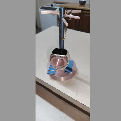 A rose gold jewelry stand with slider compartments, holding rings and a watch.