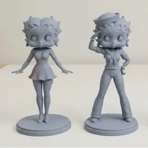 Two stylized humanoid figurines on bases; one has a dress, the other in a sailor outfit saluting.