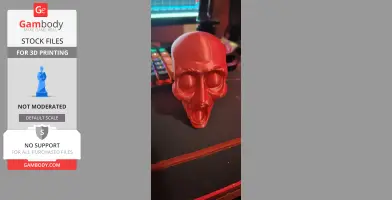 Red 3D printed skull model with large eye sockets and open mouth, placed on a desk.