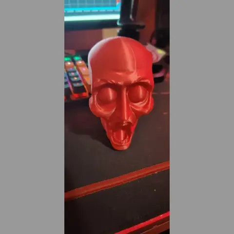 A red 3D-printed humanoid skull with an open mouth displayed on a desk.