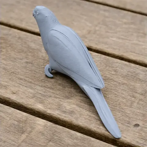 3D-printed model of a parrot with detailed feathers, sitting on a wooden surface.
