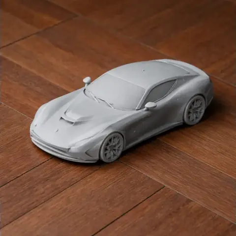 Gray 3D printed model of a sleek sports car on a wooden surface.