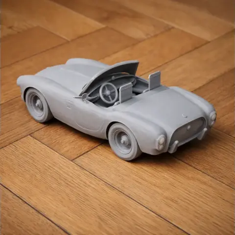 3D printed model of a classic AC Ace convertible car, detailed and unpainted, on a wooden surface.
