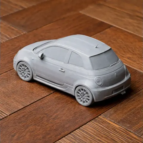 3D printed model of a compact car on a wooden surface, showcasing detailed wheels and body design.