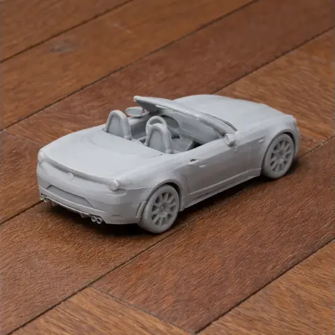 A 3D printed model of a convertible sports car, resembling an Abarth 124 Spider, on a wooden surface.