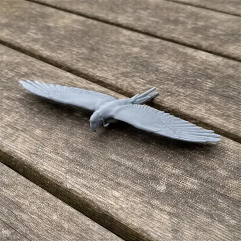 Gray 3D-printed model of a bird with outstretched wings, resembling a macaw, on a wooden surface.