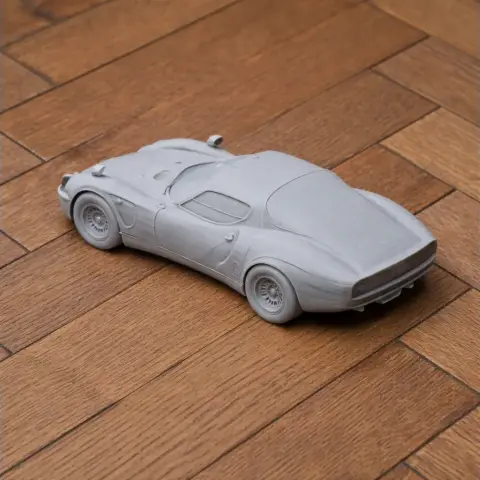 Gray 3D printed model of an Alfa Romeo 33 Stradale car on a wooden surface.