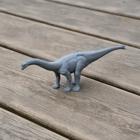 Gray 3D-printed model of a Nebulasaurus, a sauropod dinosaur, on a wooden surface.