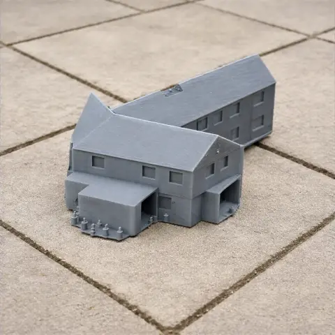 3D-printed gray model of a two-story building complex with angular roofs on a tiled surface.