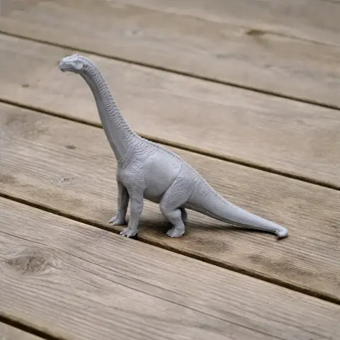 A 3D-printed model of a Neuquensaurus dinosaur, featuring a long neck and tail, on a wooden surface.