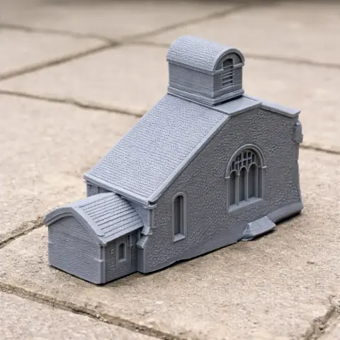 Gray 3D-printed model of a small church with arched windows and a detailed roof, on a stone surface.