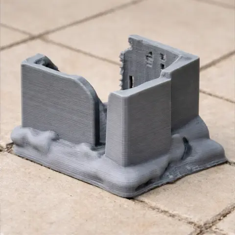 A small, gray 3D-printed model of a partially ruined tower on a textured base.