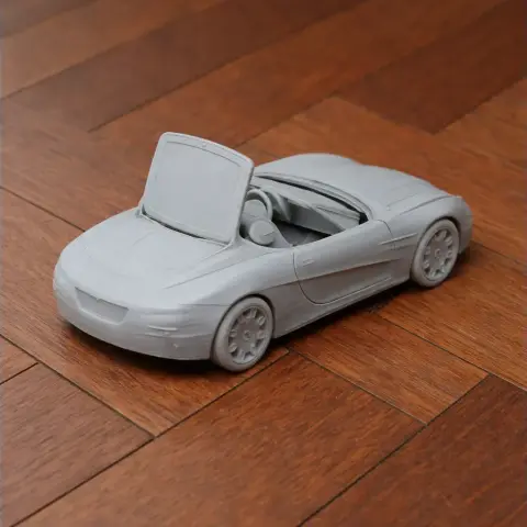 3D-printed model of a convertible sports car with an open roof, displayed on a wooden floor.
