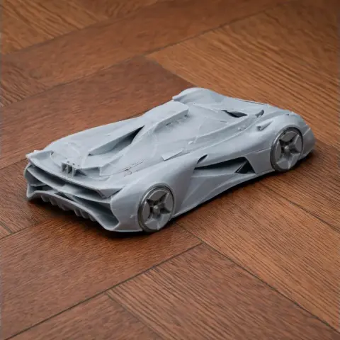 A sleek, 3D-printed scale model of a futuristic car with aerodynamic design, placed on a wooden floor.