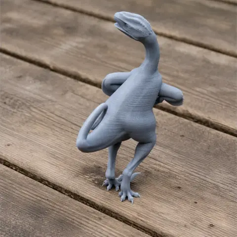 Gray 3D-printed model of Ornitholestes, a bipedal prehistoric dinosaur, posed on a wooden surface.