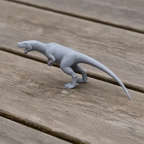 Gray 3D-printed model of a dinosaur with a long tail and open mouth on a wooden surface.