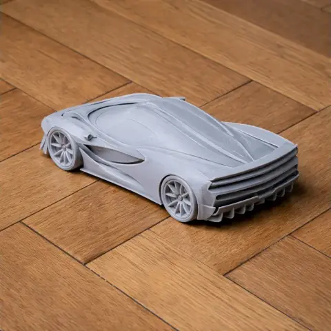 A sleek, gray 3D-printed model of a futuristic sports car on a wooden surface.