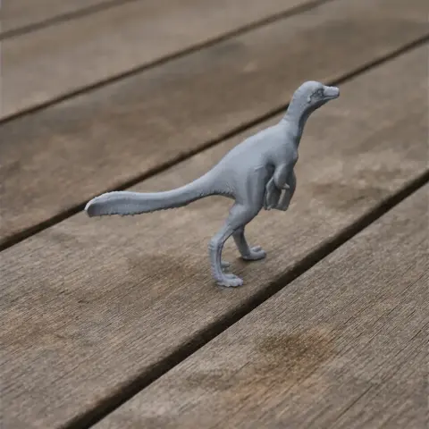 A small, gray 3D-printed model of a Philovenator dinosaur on a wooden surface.