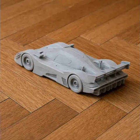 A detailed 3D-printed model of a sleek racing car on a wooden floor.